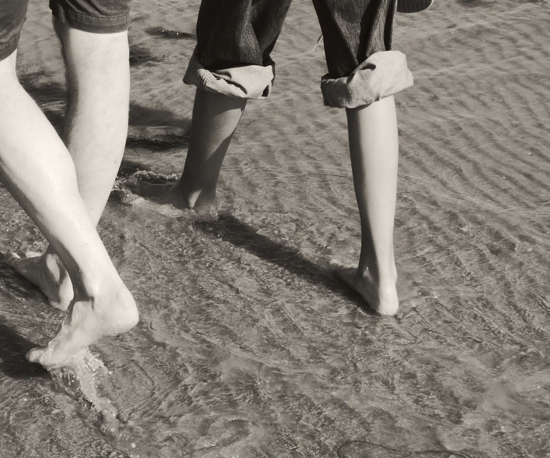Two people walking barefoot side by side across wet sand
